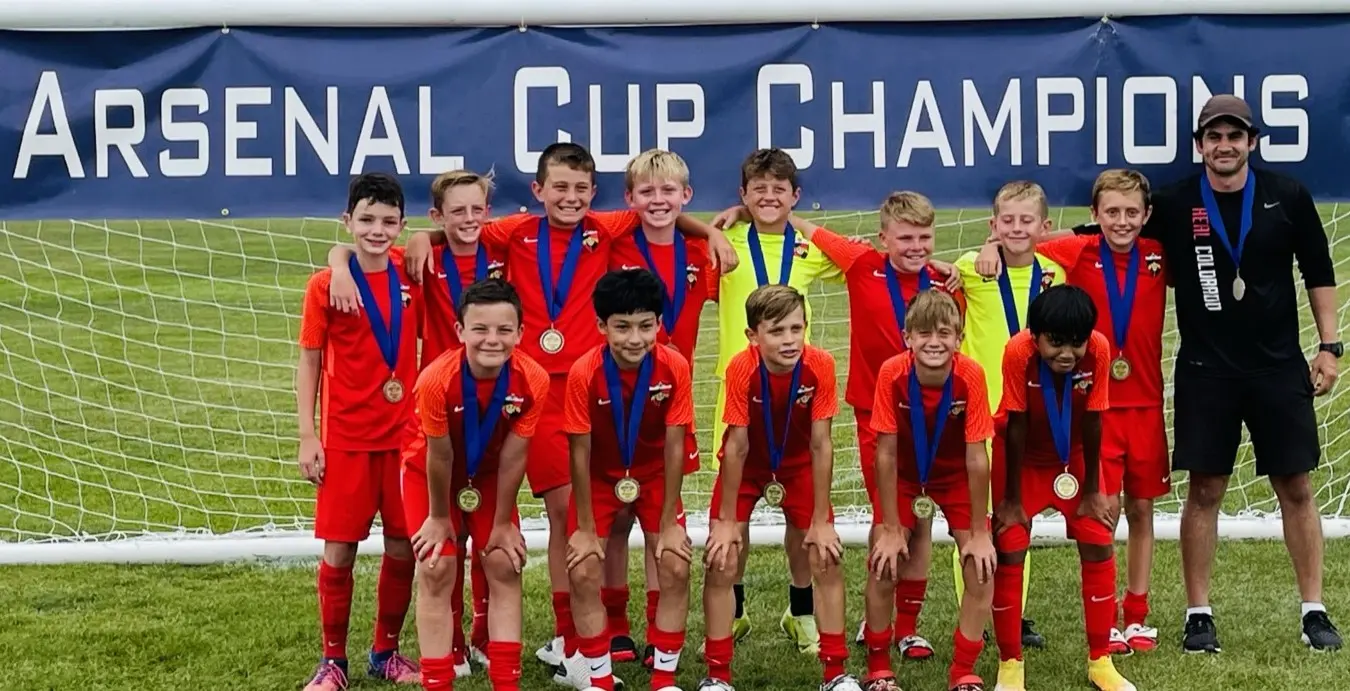 Real Colorado Academy team in white and grey SG kits with medals in front of Kick It 3v3 banner August 2022